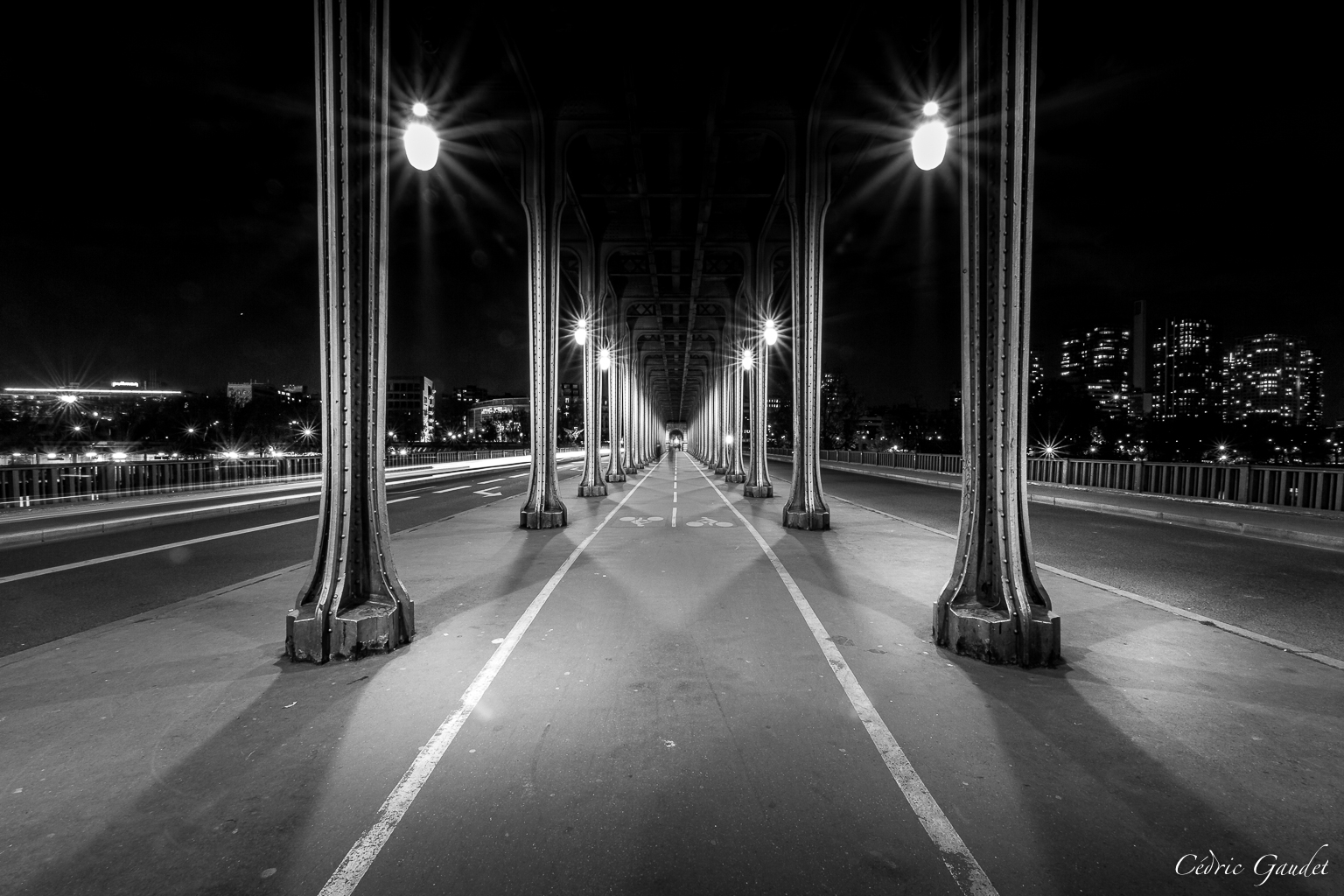 Vue nocturne d'un pont en béton et en acier, illuminé par des réverbères, avec des colonnes majestueuses encadrant la chaussée et offrant une perspective unique.