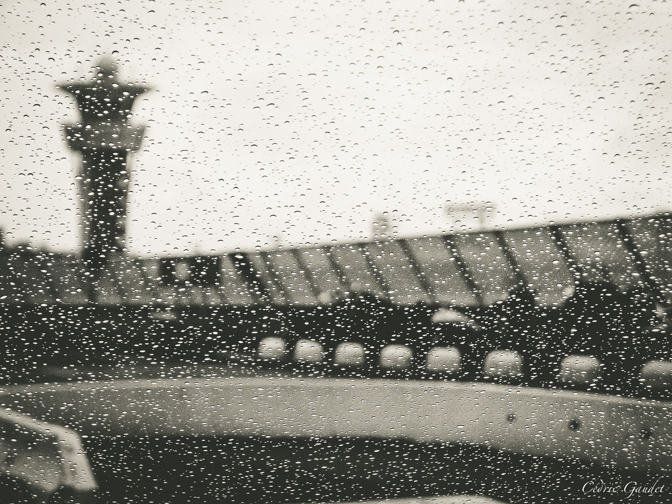 Gouttes de pluie sur une vitre avec une silhouette floue en arrière-plan, illustrant une atmosphère mélancolique.