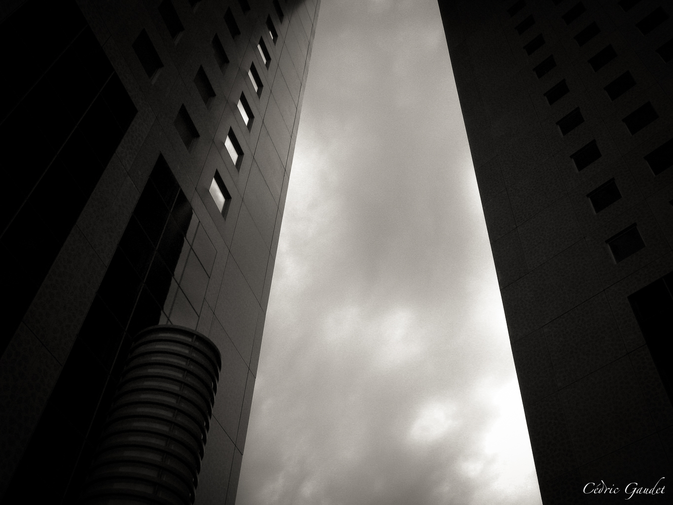 Vue en contre-plongée de deux bâtiments modernes en béton, acier et verre, avec un ciel nuageux en arrière-plan.
