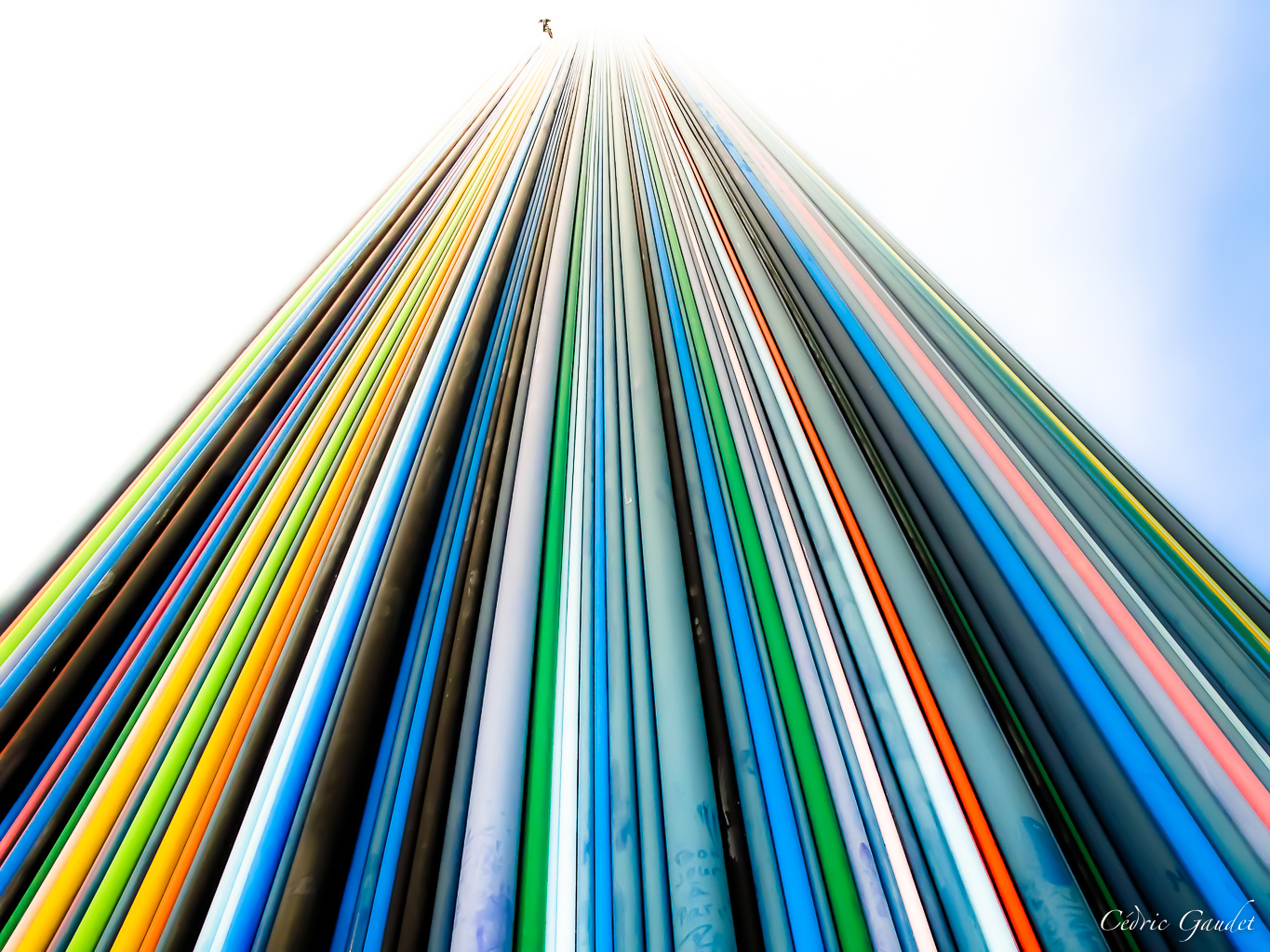 Vue en contre-plongée de plusieurs colonnes colorées alignées verticalement, avec un ciel clair en arrière-plan.