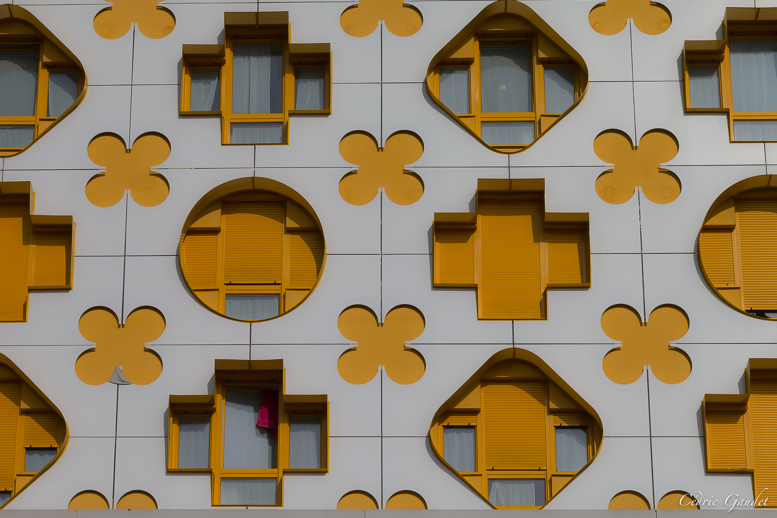 Façade d'immeuble avec motifs géométriques en jaune et blanc, présentant des fenêtres de différentes formes et tailles.